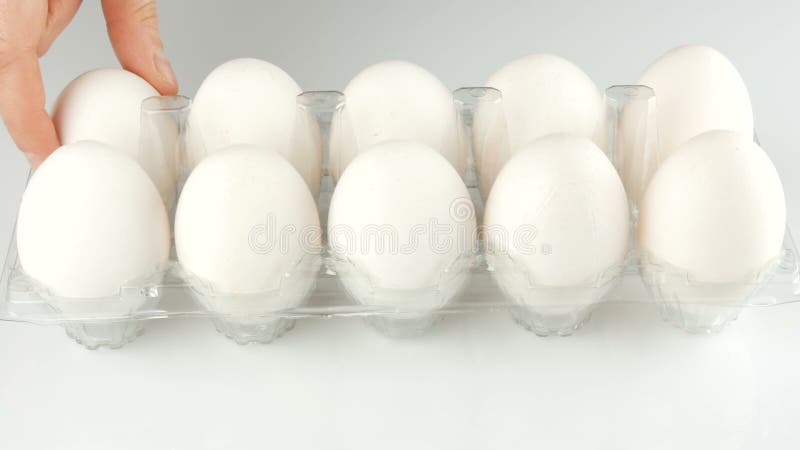 Μεγάλα άσπρα αυγά κοτόπουλου σε έναν διαφανή πλαστικό δίσκο σε ένα άσπρο υπόβαθρο Τα θηλυκά χέρια αγγίζουν κάθε τα αυγά